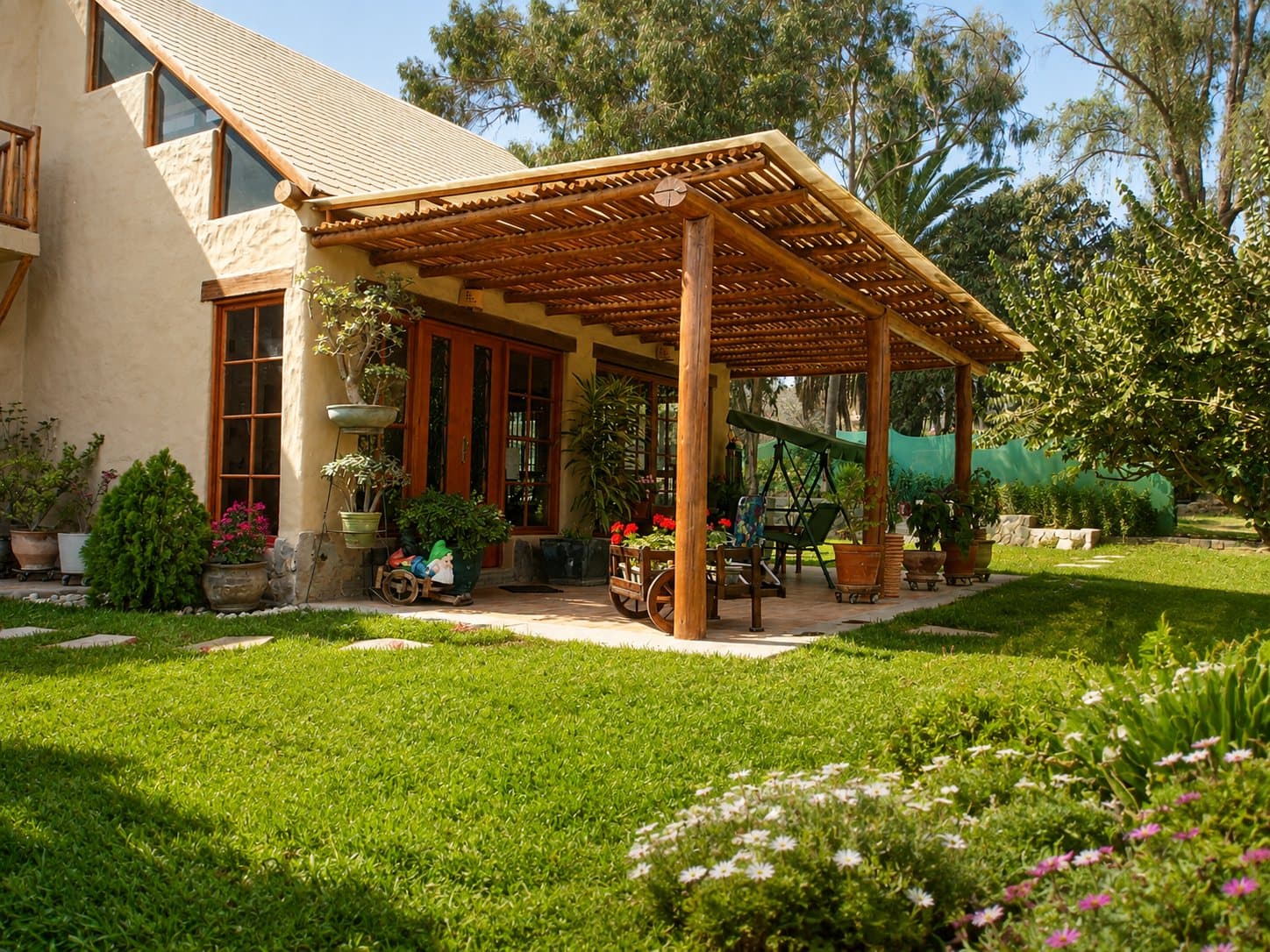 Pérgola de madera, jardín florido y muros de tierra en una casa construida por ECORAIZ
